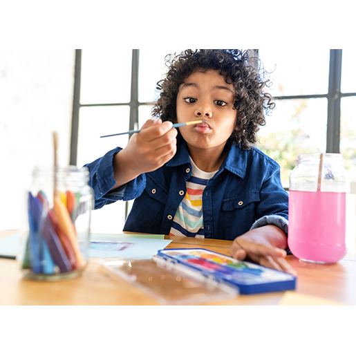 A little boy holds a paintbrush in front of his nose